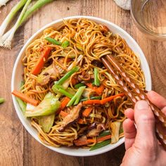 someone is holding chopsticks over a bowl of noodles with chicken and veggies