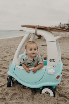 a baby sitting in a toy car on the beach