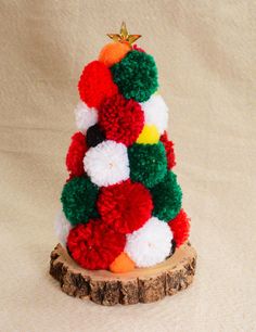 a multicolored christmas tree made out of pom - poms sits on a piece of wood