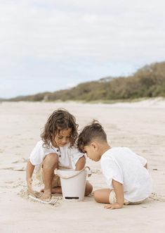 two young children playing in the sand with a bucket and spadel at the beach