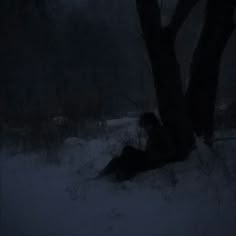 a person laying in the snow under a tree at night with their head turned to the side