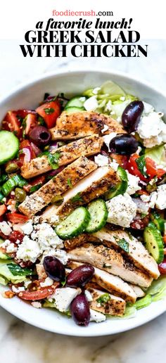 a white bowl filled with chicken, cucumber and olives on top of a table