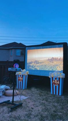 an outdoor movie screen with popcorn buckets in the foreground and two movies on the back