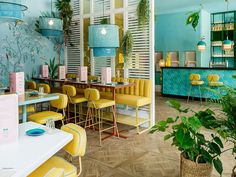 the interior of a restaurant with blue walls and yellow chairs, potted plants on the tables