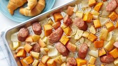 sausage, potatoes and croissants in a baking pan on a white table