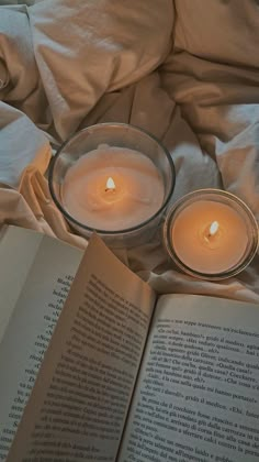 an open book sitting on top of a bed next to two lit candles in a glass bowl