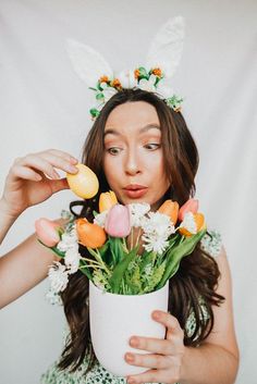 a woman holding a vase with flowers in it and an easter bunny ears on her head