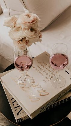 two wine glasses sitting on top of a book next to a vase with flowers in it