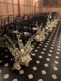 rows of black chairs with white flowers and greenery lined up on the floor in front of them