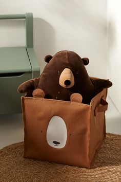 a teddy bear sitting in a brown bag on the floor next to a green chair