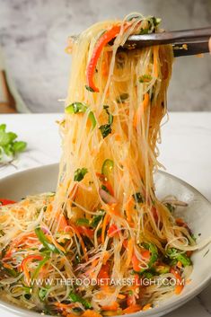 someone is lifting noodles from a bowl with chopsticks to eat the food on the plate