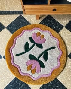 a rug with pink flowers on it in the middle of a floor next to a dresser