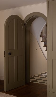 an arched door in the entry way to a house with stairs and checkerboard flooring