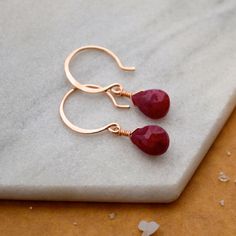 Make a bold but understated statement with our Sookie Earrings. These Ruby earrings feature faceted gems in a crimson red hue. We hand wire-wrap the gemstones in our signature tightrope style, anchored beneath our classic lure earwires. A perfect pop of color! Choose from affordable Gold Fill, Sterling Silver, and Rose Gold Fill; or heirloom-quality solid 14K Gold (Yellow, Rose, or White Gold). Our sustainable jewelry is water resistant - safe for the shower or sea. Details: Gemstone: Ruby Full Rose Gold Teardrop Ruby Jewelry, Dainty Red Earrings For Everyday, Red Drop Earrings For Everyday Wear, Red 14k Gold-filled Gemstone Jewelry, Red 14k Gold Filled Drop Earrings, Dainty Red Jewelry With Ear Wire, Minimalist Jewelry Earrings, Drop Earrings Simple, Nautical Inspiration