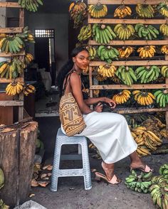 a woman sitting on a stool next to bunches of bananas