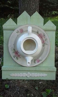 a white vase sitting on top of a green box next to a tree and grass