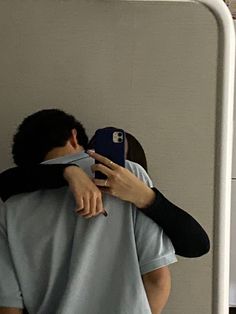 two people are hugging each other in front of a mirror and one person is wearing a baseball cap