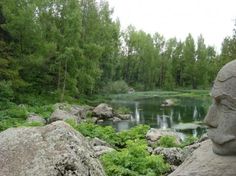 there is a statue in the middle of some rocks and plants near a lake with trees around it