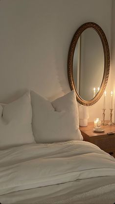 a bed with white sheets and pillows in front of a round mirror