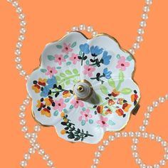 a decorative white plate with flowers and pearls on an orange background that looks like something out of nowhere