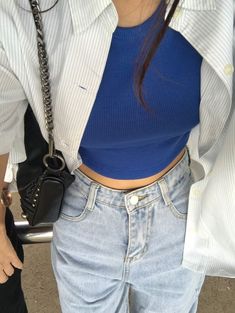 a woman in blue shirt and jeans holding a black purse