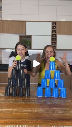 two girls are playing with plastic cups in the kitchen