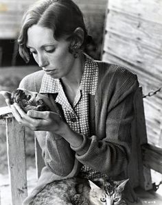 a woman sitting on a bench holding a cat and looking at something in her hand