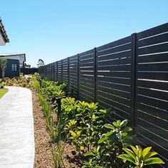 a long black fence is next to some plants and bushes in front of a house