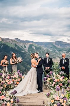 a bride and groom kissing in front of their wedding party at the top of a mountain