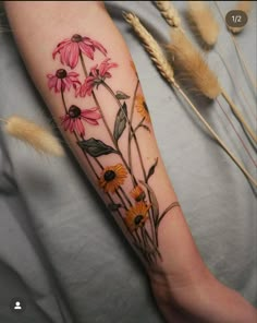 a woman's arm with flowers on it and some feathers in the foreground