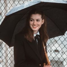 a young woman holding an umbrella in front of a chain link fence smiling at the camera