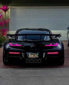 two black sports cars parked in front of a garage with pink flowers on the driveway