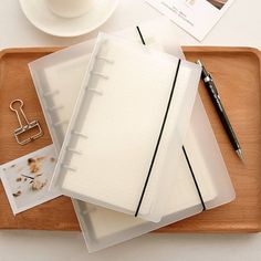 a wooden tray topped with three binders next to a cup of coffee and a pen