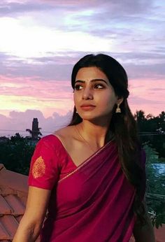 a woman in a pink sari standing on top of a roof with the sun setting behind her