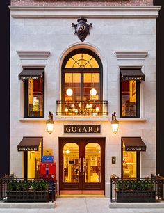 the front entrance of a building with many windows and plants in pots on the sidewalk