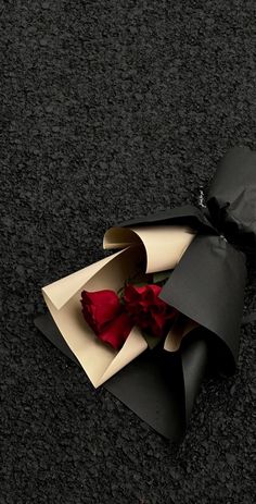 an open black paper bag with a red rose in it on the ground next to a pair of gloves