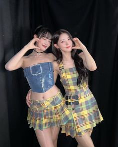 two young women posing for the camera in front of a black background wearing plaid outfits