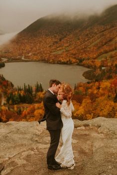 a bride and groom kissing on top of a mountain with fall foliage in the background