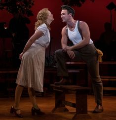 a man and woman sit on a bench in front of a red background while one looks at the other