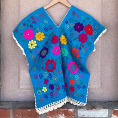 a blue top with colorful flowers on it hanging from a brick wall next to a wooden hanger