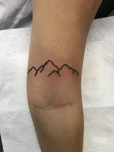 a tattoo on the leg of a person with mountains in the background and black ink