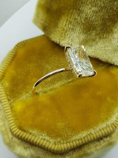 an engagement ring sitting on top of a yellow velvet cushioned case with a diamond set in the center