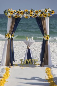 an outdoor wedding setup on the beach with sunflowers and blue draping