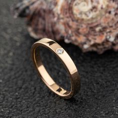 a gold wedding ring with a diamond on the side and a seashell in the background