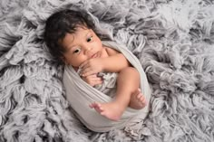 a baby wrapped up in a blanket on top of a gray blanket, looking at the camera