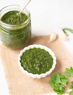 a small white bowl filled with green pestle next to a jar full of pesto