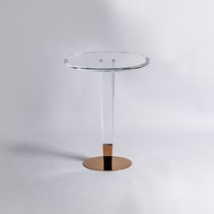 a round glass table with a gold base on a plain white surface in front of a grey background