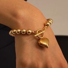 Elevate your everyday look with our Roman Heart Charm Bracelet. This chic and stylish golden beaded bracelet is perfect for all-day wear, and the dangle heart charm adds a touch of charm. Perfect as a gift or for treating yourself to a little luxury. Size: 7.5" Width: 8mm beads Charm: 1.75cm x 1.75cm Material: Stainless Steel Plating: 18k real gold Toddle Closure Pair with Roman Oversized Heart Necklace for a matching set. Metal Heart-shaped Beaded Bracelets For Valentine's Day, Heart-shaped Metal Beaded Bracelets For Valentine's Day, Metal Heart-shaped Beaded Bracelet For Valentine's Day, Elegant Heart-shaped Metal Beaded Bracelets, Gold Metal Charm Bracelet With Heart Beads, Elegant Metal Beaded Bracelet With Heart Charm, Elegant Metal Beaded Bracelets For Valentine's Day, Gold Dangle Charm Bracelet With Heart Charm, Elegant Beaded Bracelet With Heart Charm For Valentine's Day