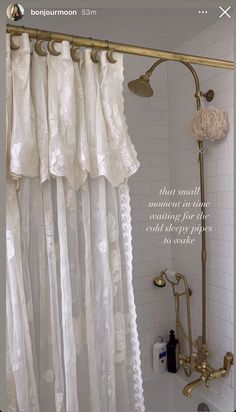 the shower curtain is white and has gold hardware on it, along with an antique brass faucet