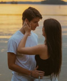 a young man and woman standing next to each other near the water at sunset or sunrise